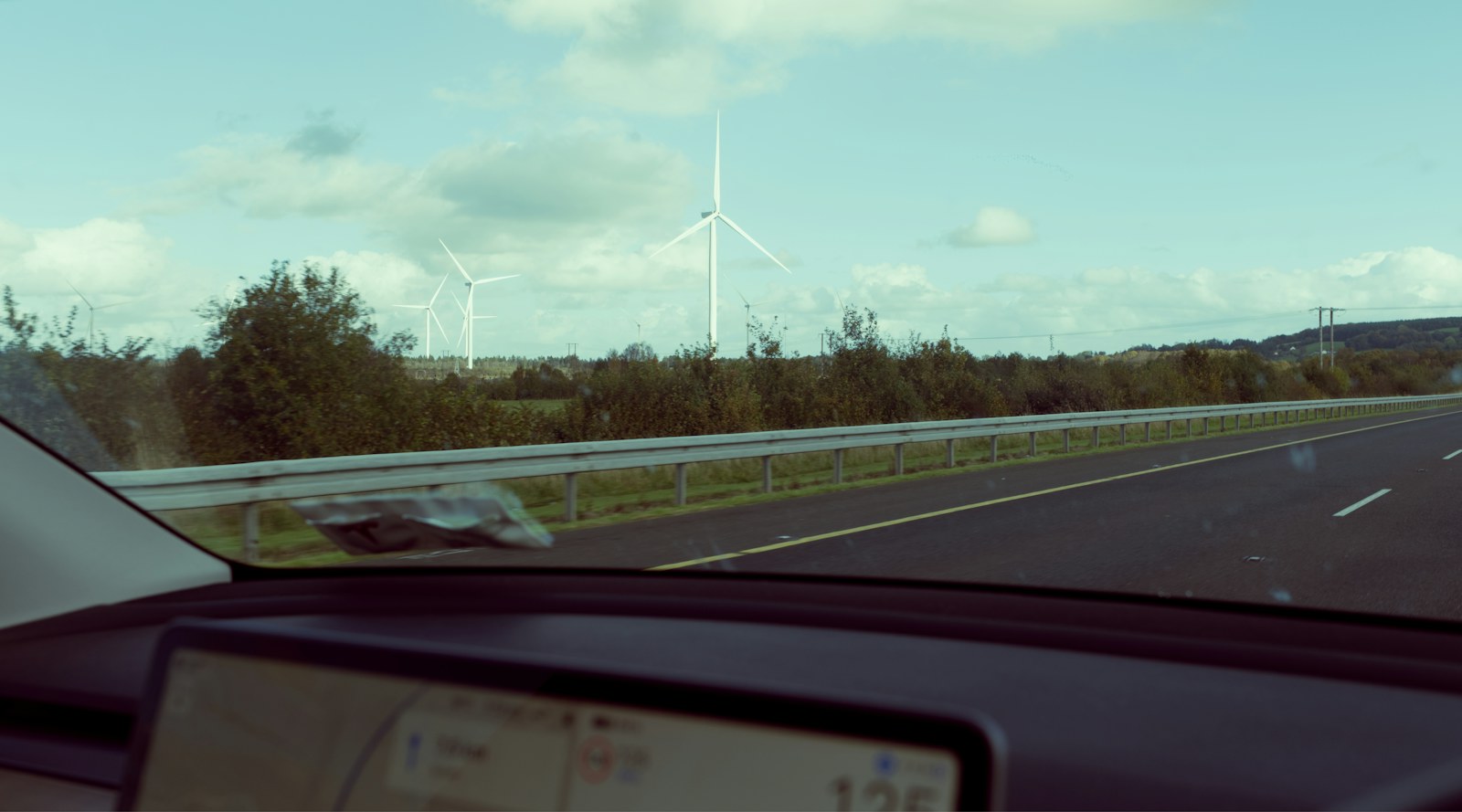 A motorway and wind turbine seen through a car windscreen. Illustrative image