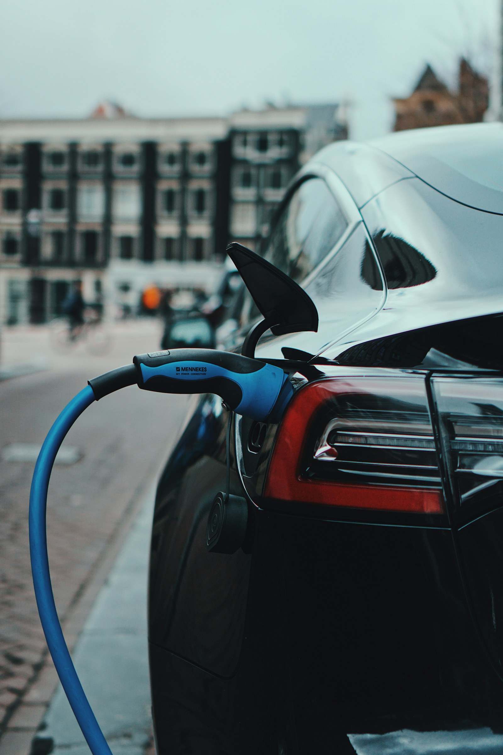 A black electric car charging on a city street. Illustrative image